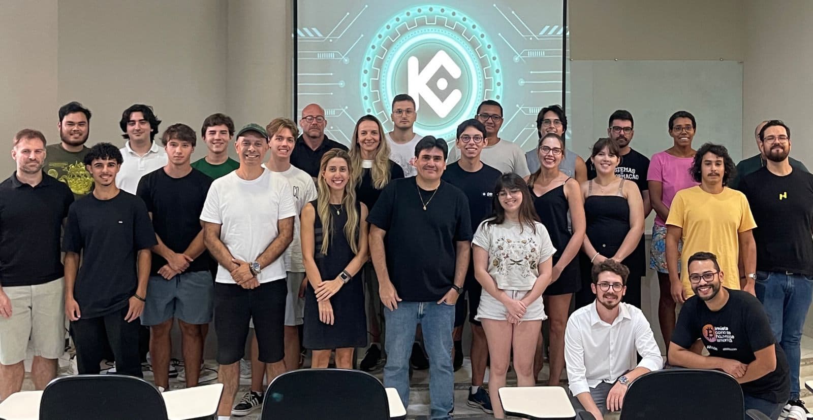 Participantes do meetup KuCoin em Florianópolis diante do telão com o logo da KuCoin